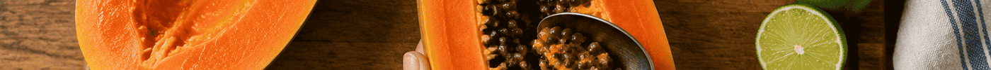 Hand scraping seeds from a halved papaya on a wooden board